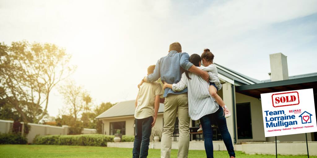 A happy family with two kids are standing in front of the house they just bought